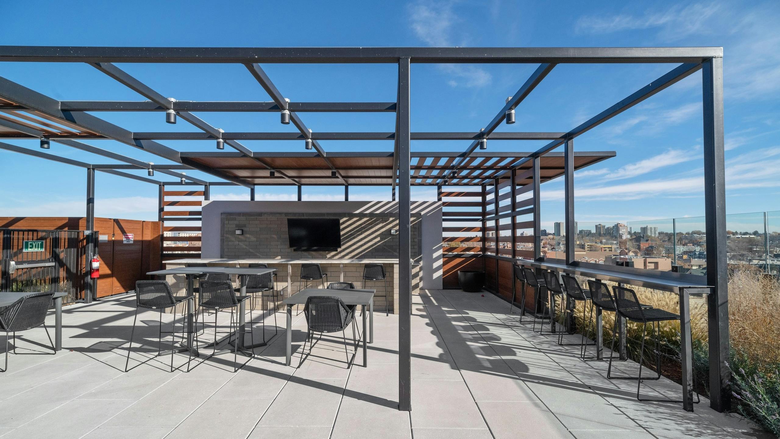 AMLI at Uptown rooftop bar amenity space with a metal pergola structure over seating areas surrounded by bright city views