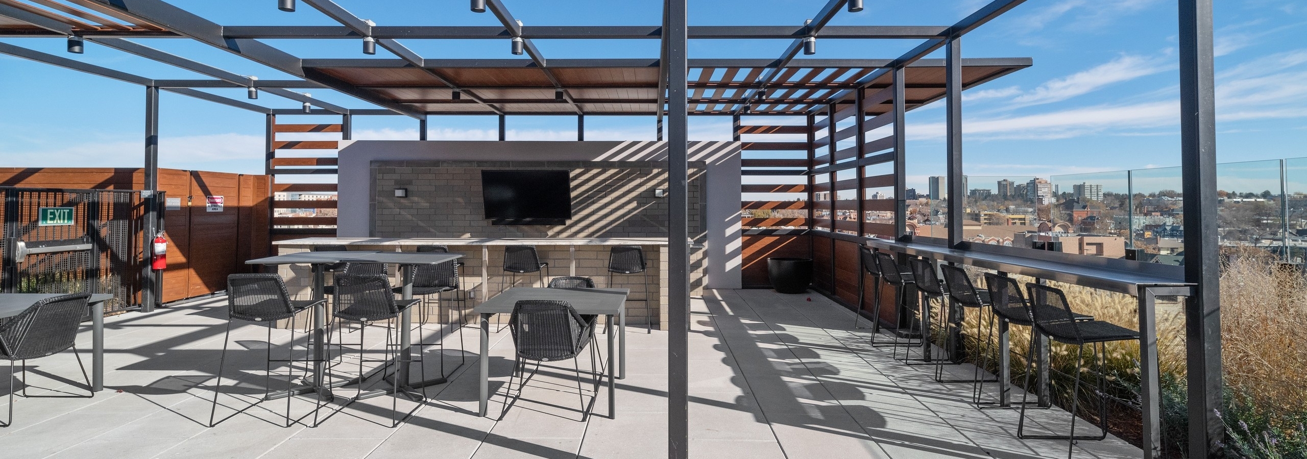 AMLI at Uptown rooftop bar amenity space with a metal pergola structure over seating areas surrounded by bright city views