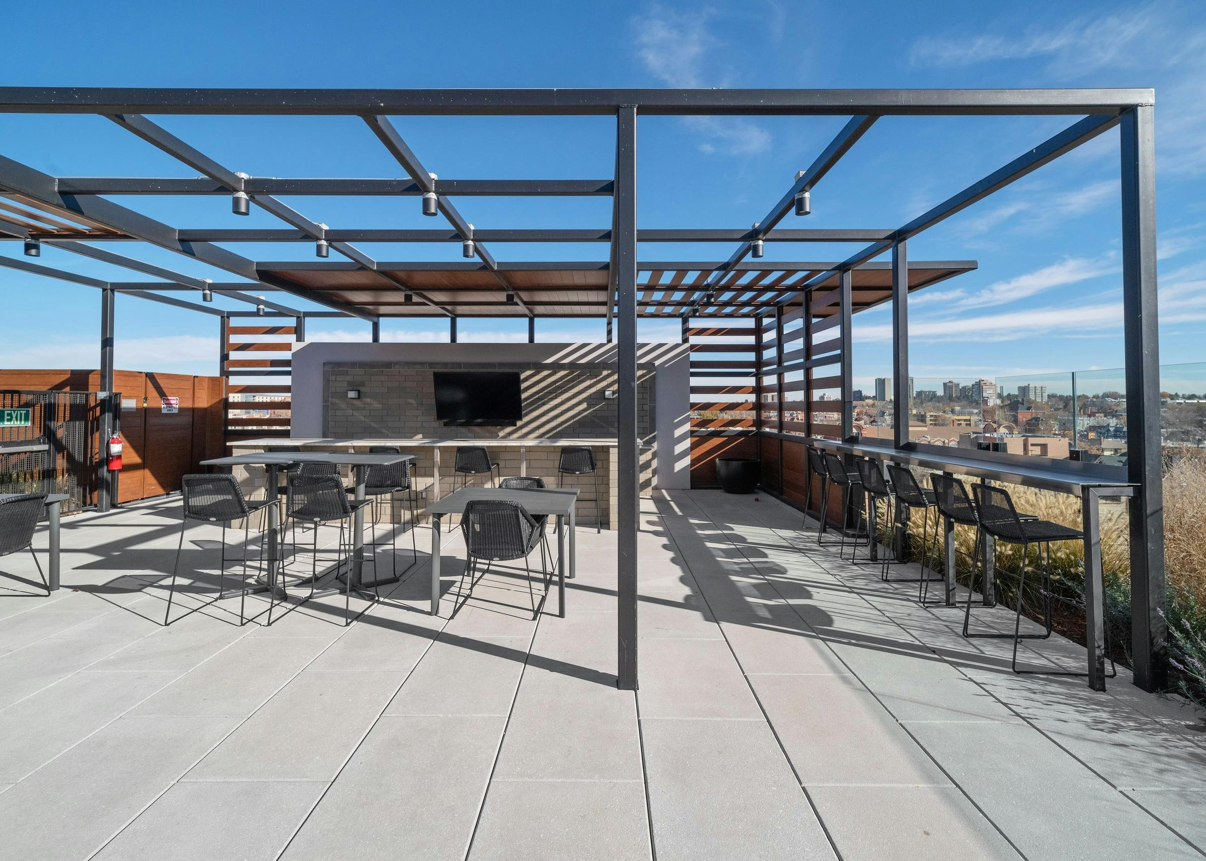 AMLI at Uptown rooftop bar amenity space with a metal pergola structure over seating areas surrounded by bright city views