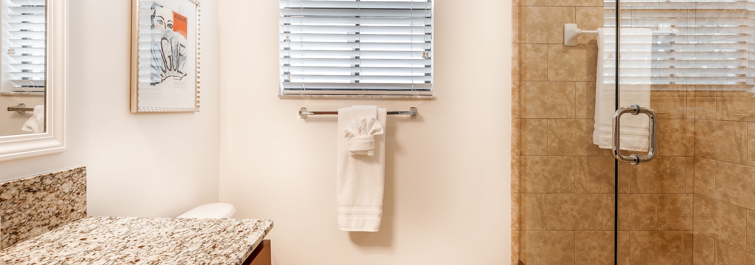 AMLI Toscana Place apartment bathroom with glass shower with beige tile wall with a side window and artwork above toilet