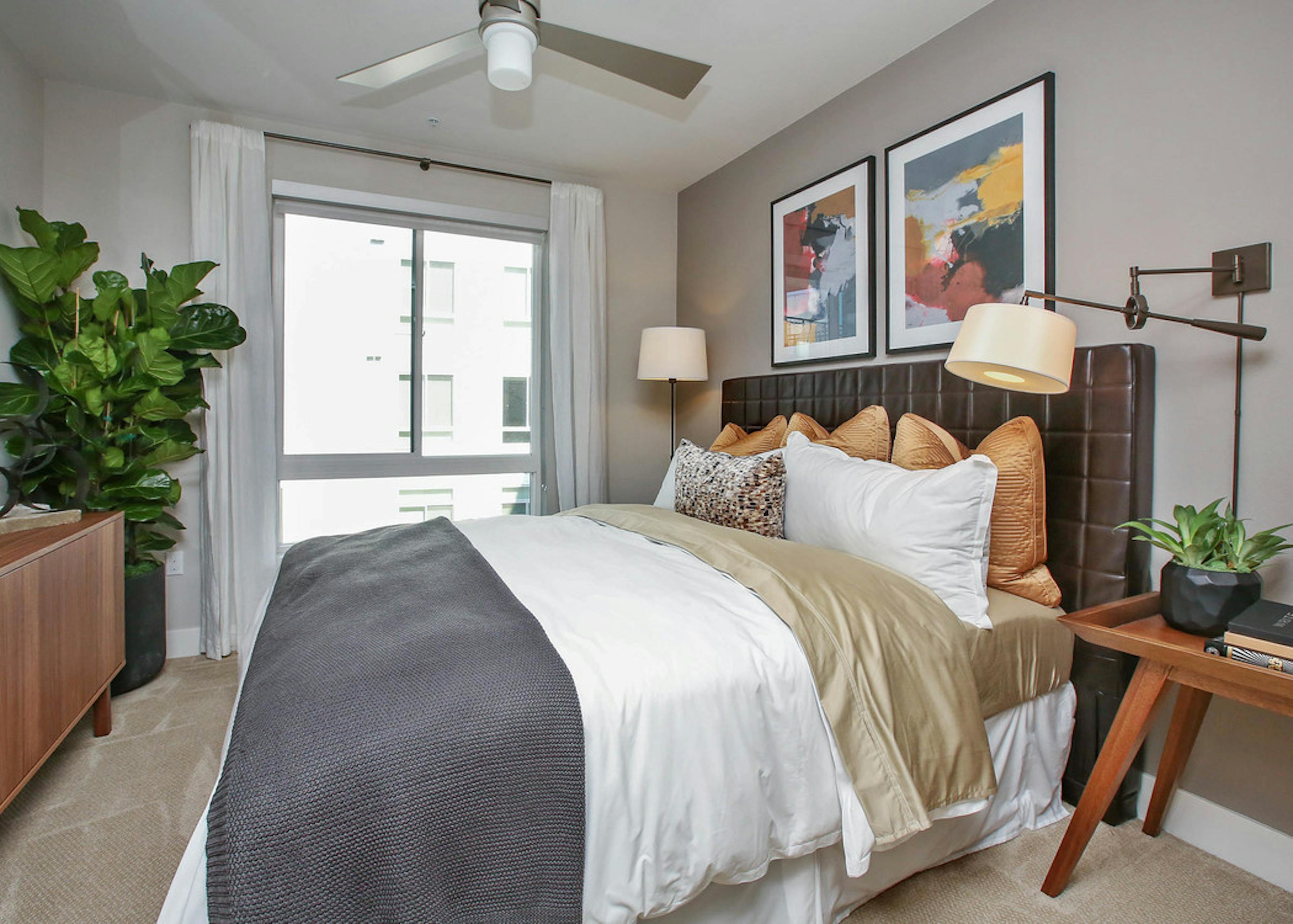 Interior of AMLI Uptown Orange apartment bedroom with king bed with grey walls and night stand in front of large window