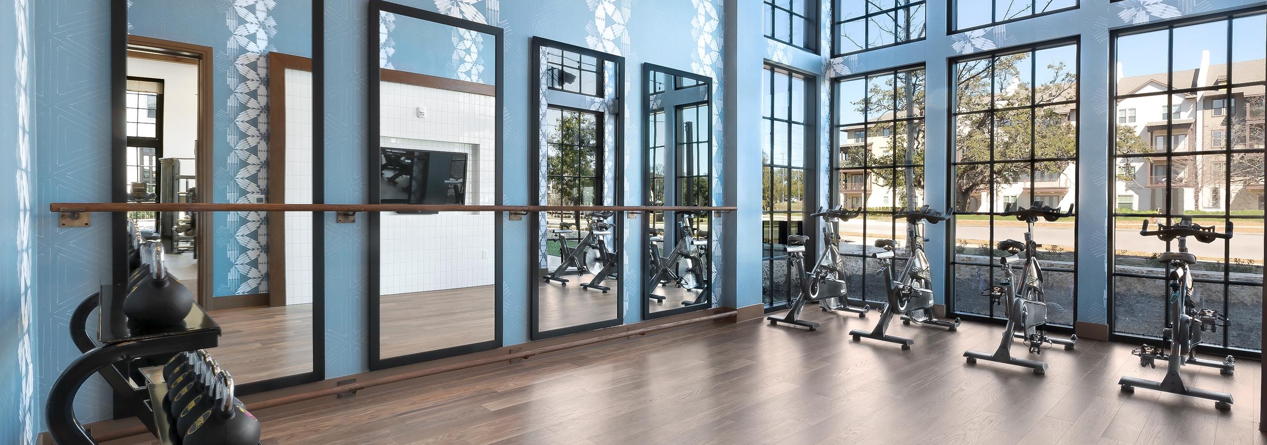 Daytime view of yoga and spin room at AMLI Lakeline with free weights and stationed bicycles facing floor to ceiling windows