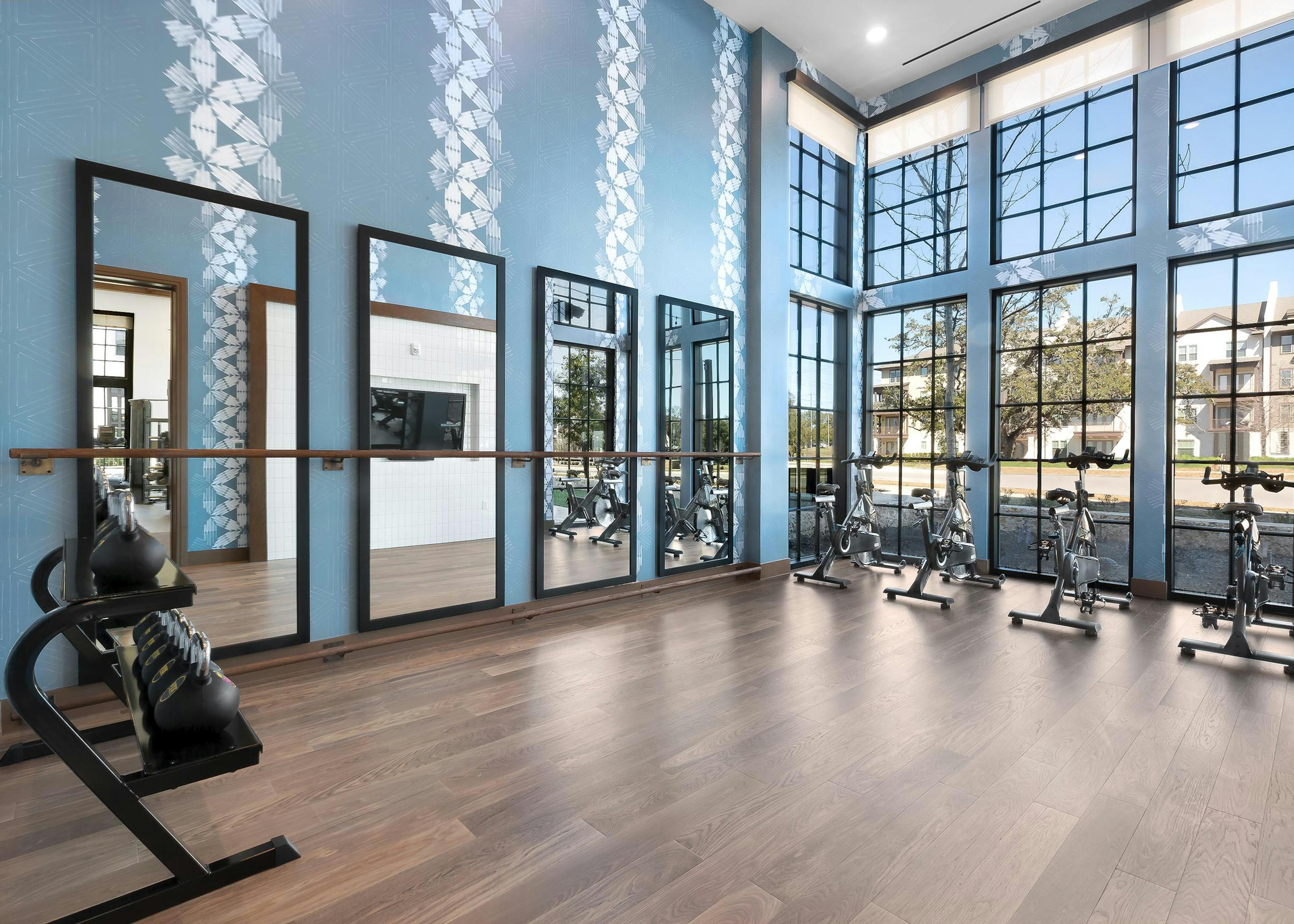 Daytime view of yoga and spin room at AMLI Lakeline with free weights and stationed bicycles facing floor to ceiling windows