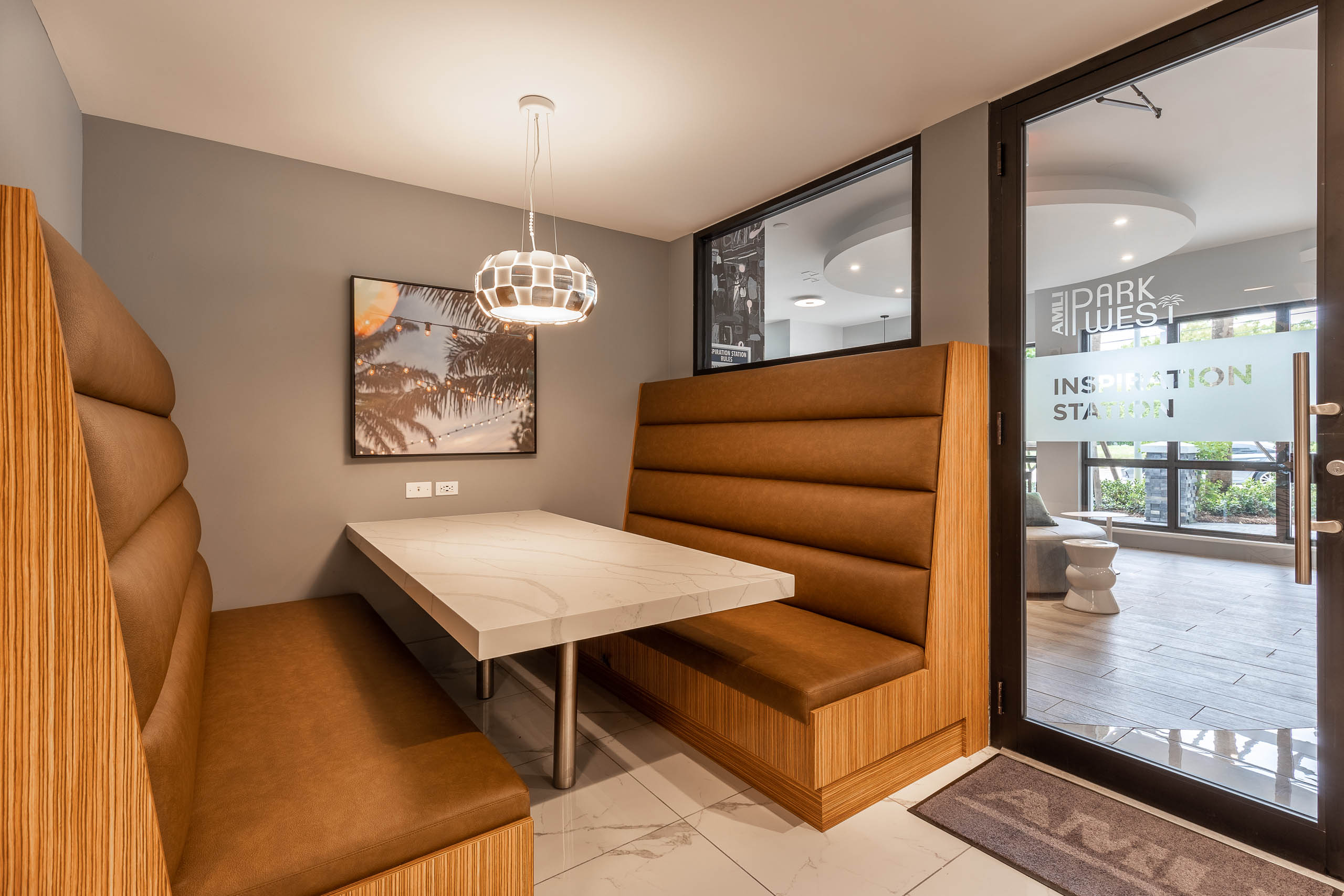 Entry to the AMLI Park West apartments inspiration station lounge with brown leather booth seat and table with hanging light 