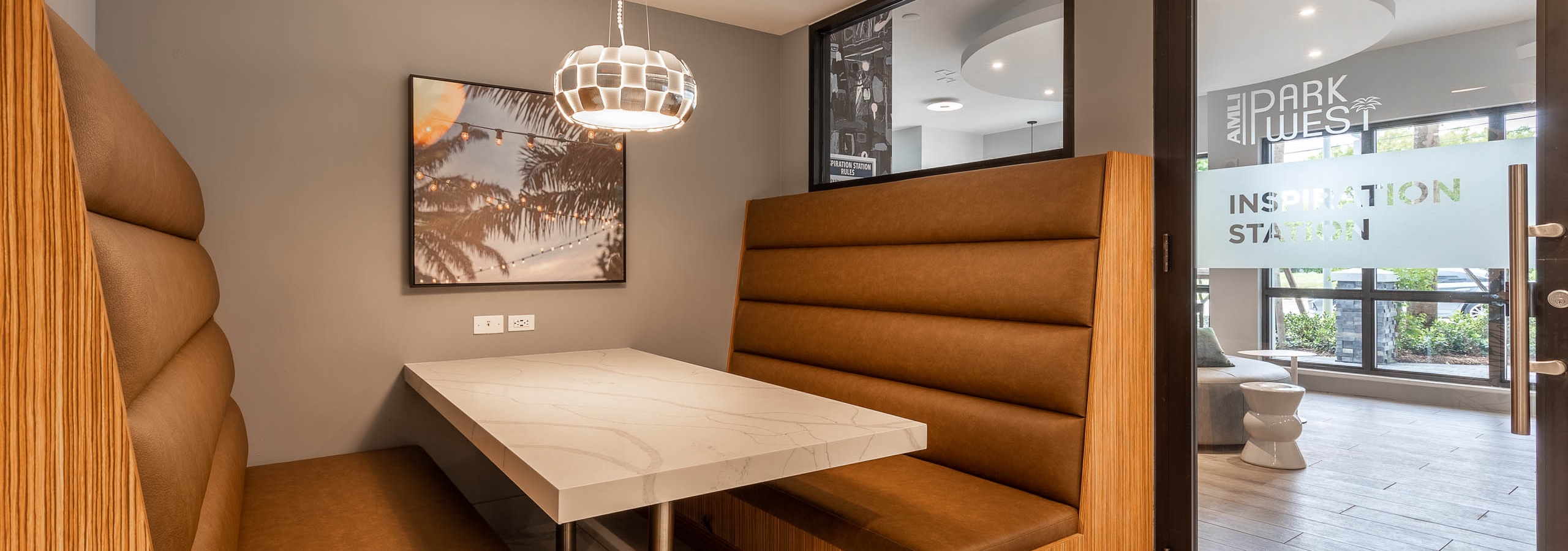 Entry to the AMLI Park West apartments inspiration station lounge with brown leather booth seat and table with hanging light