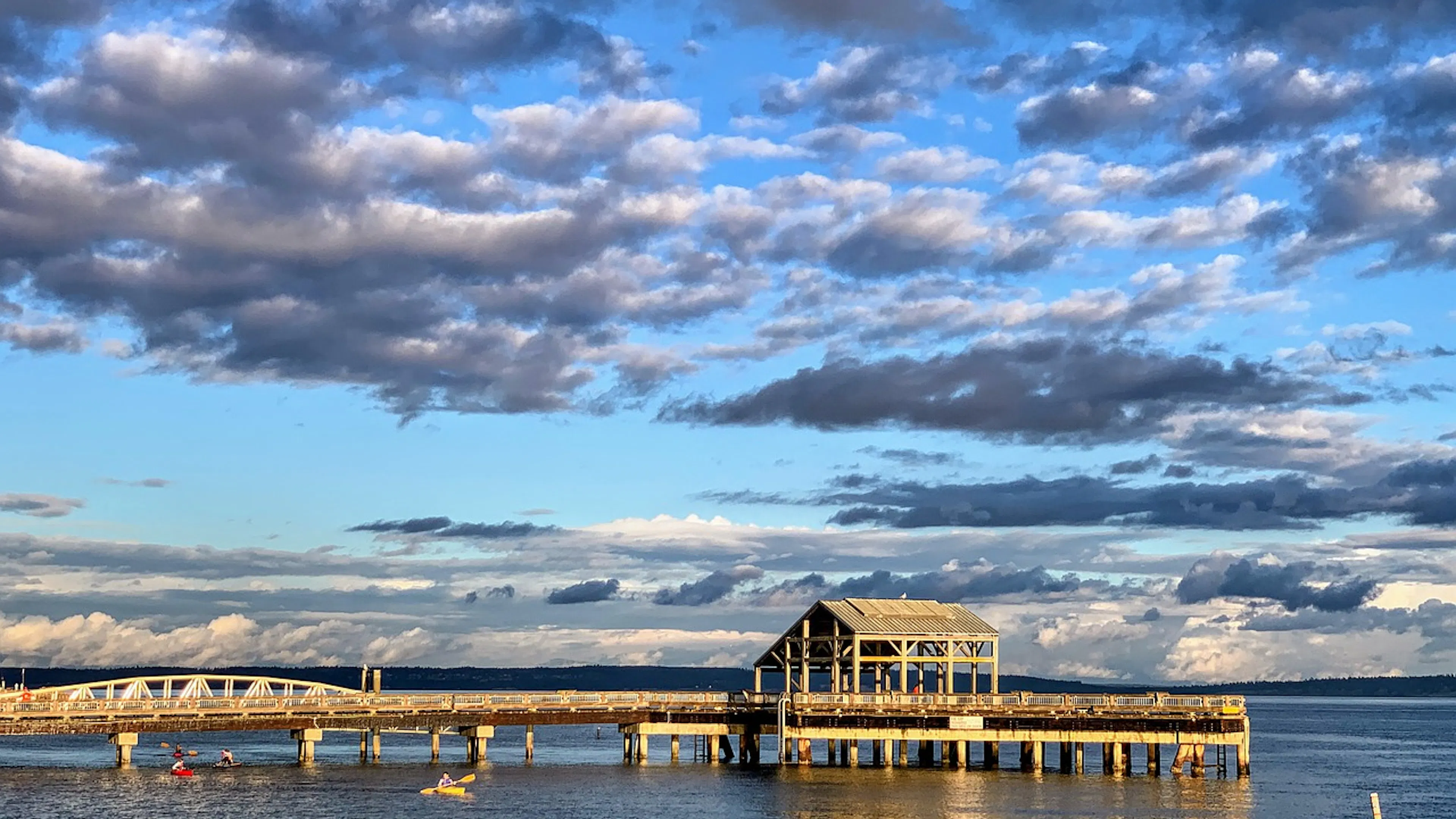 A pier sticking out onto the Puget Sound with an island and dark clouds in the background