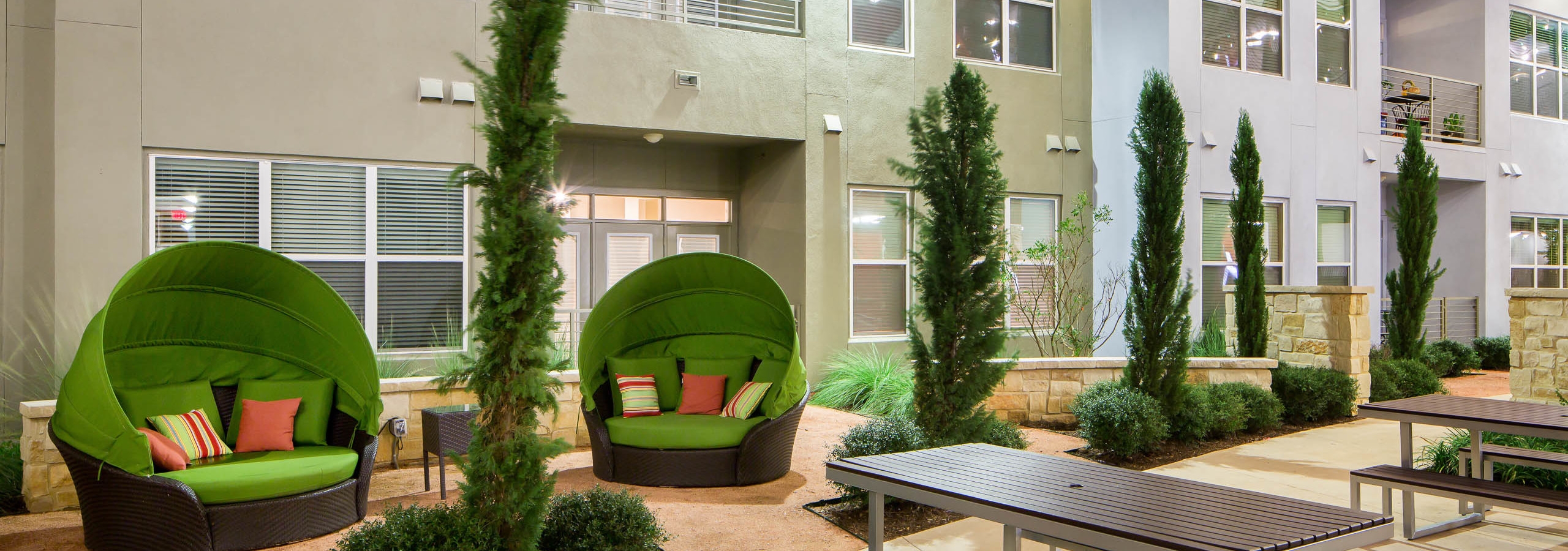 Close up of covered green moon chairs with colorful pillows in the courtyard at AMLI at Mueller apartment community