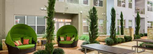 Close up of covered green moon chairs with colorful pillows in the courtyard at AMLI at Mueller apartment community