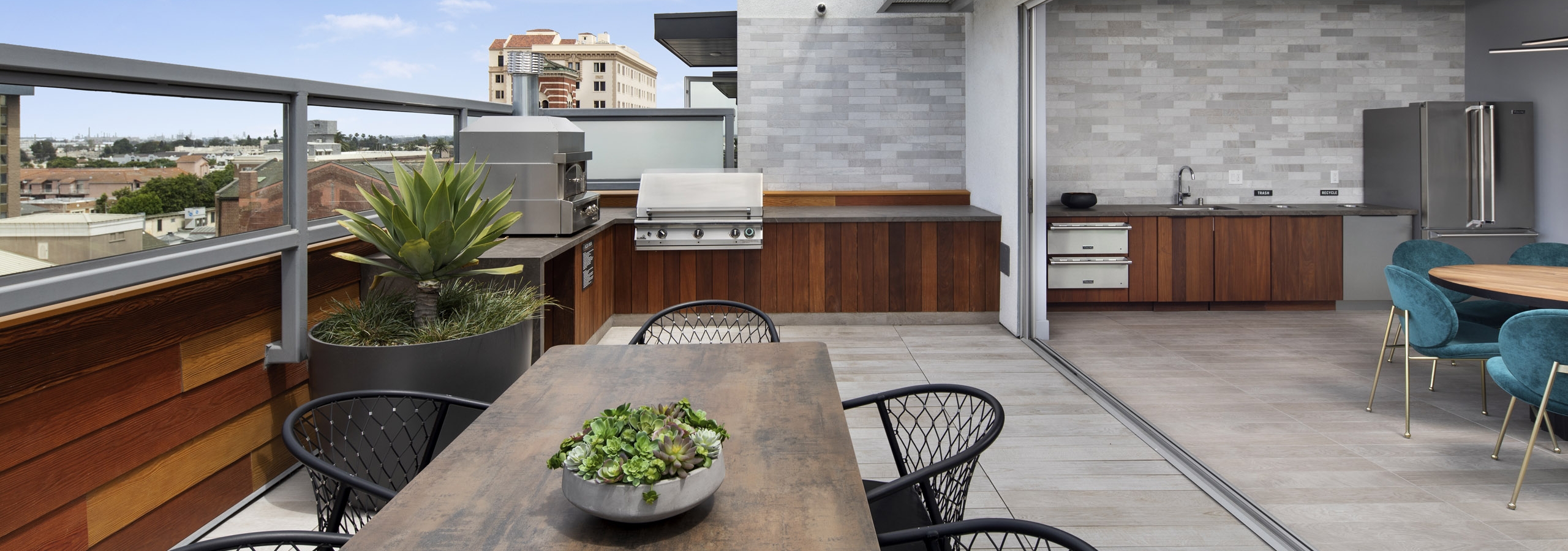 Exterior daytime view of rooftop lounge with BBQ grill and pizza oven and tables and chairs overlooking the city