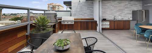 Exterior daytime view of rooftop lounge with BBQ grill and pizza oven and tables and chairs overlooking the city