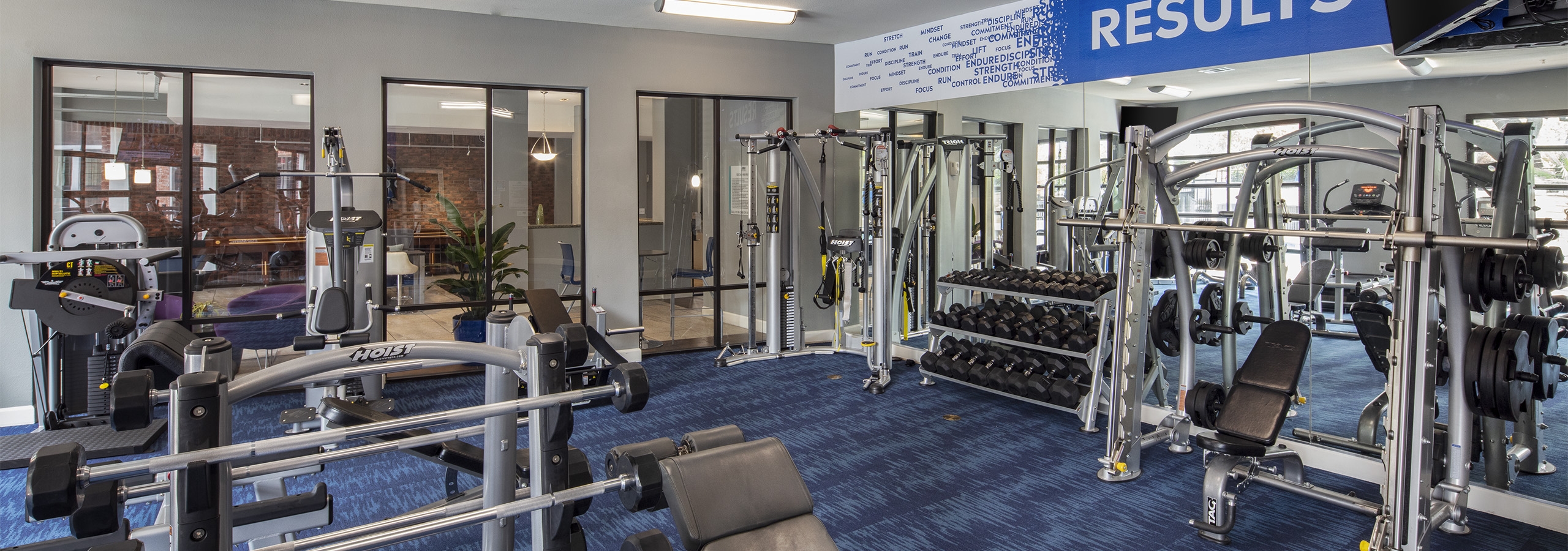 Fitness center at AMLI Eastside apartments with strength training  machines and a dumbbell rack set on patterned blue carpet