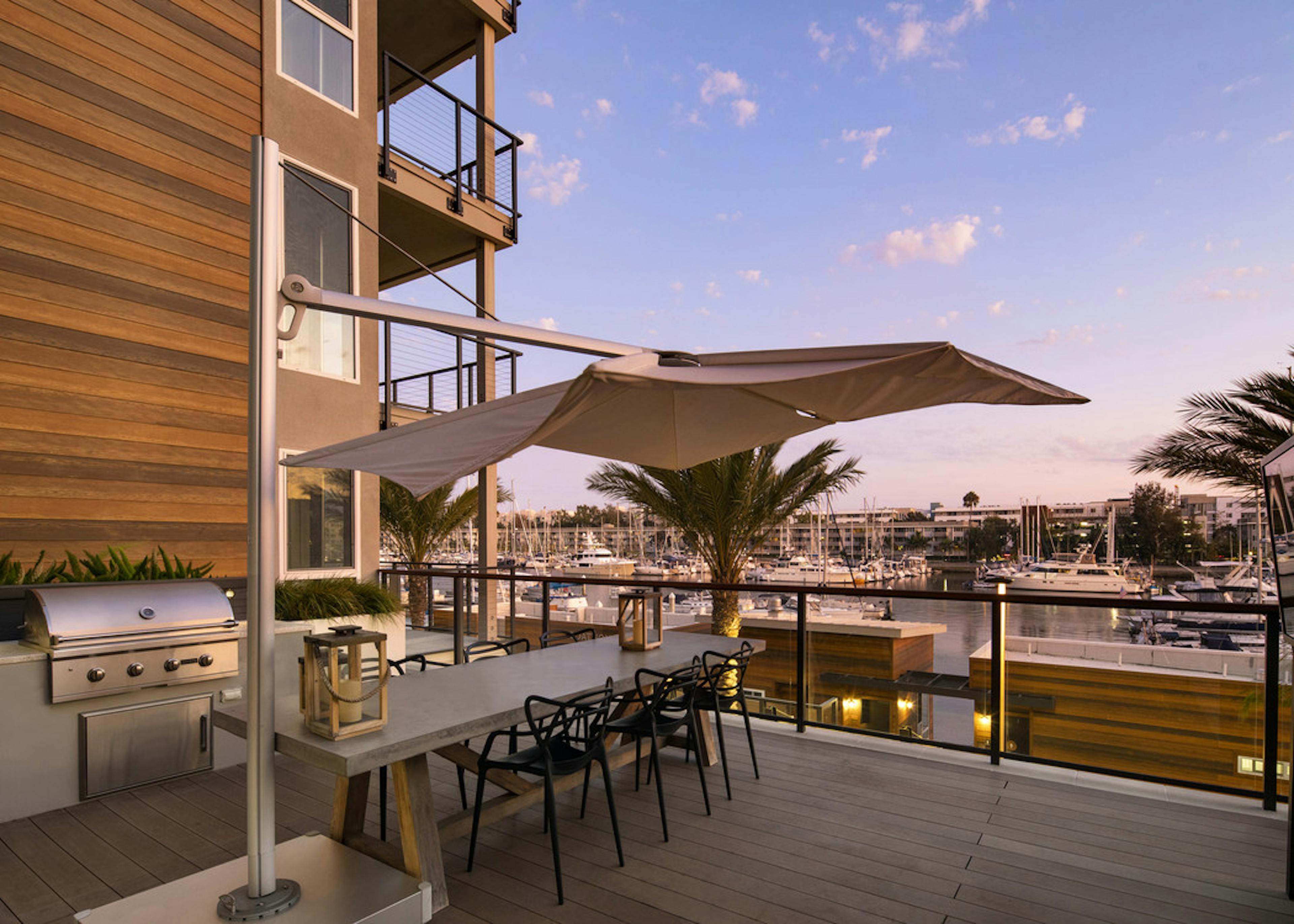 Daytime view of lounge deck with table and umbrella and grill station overlooking the peaceful marina at AMLI Marina Del Rey
