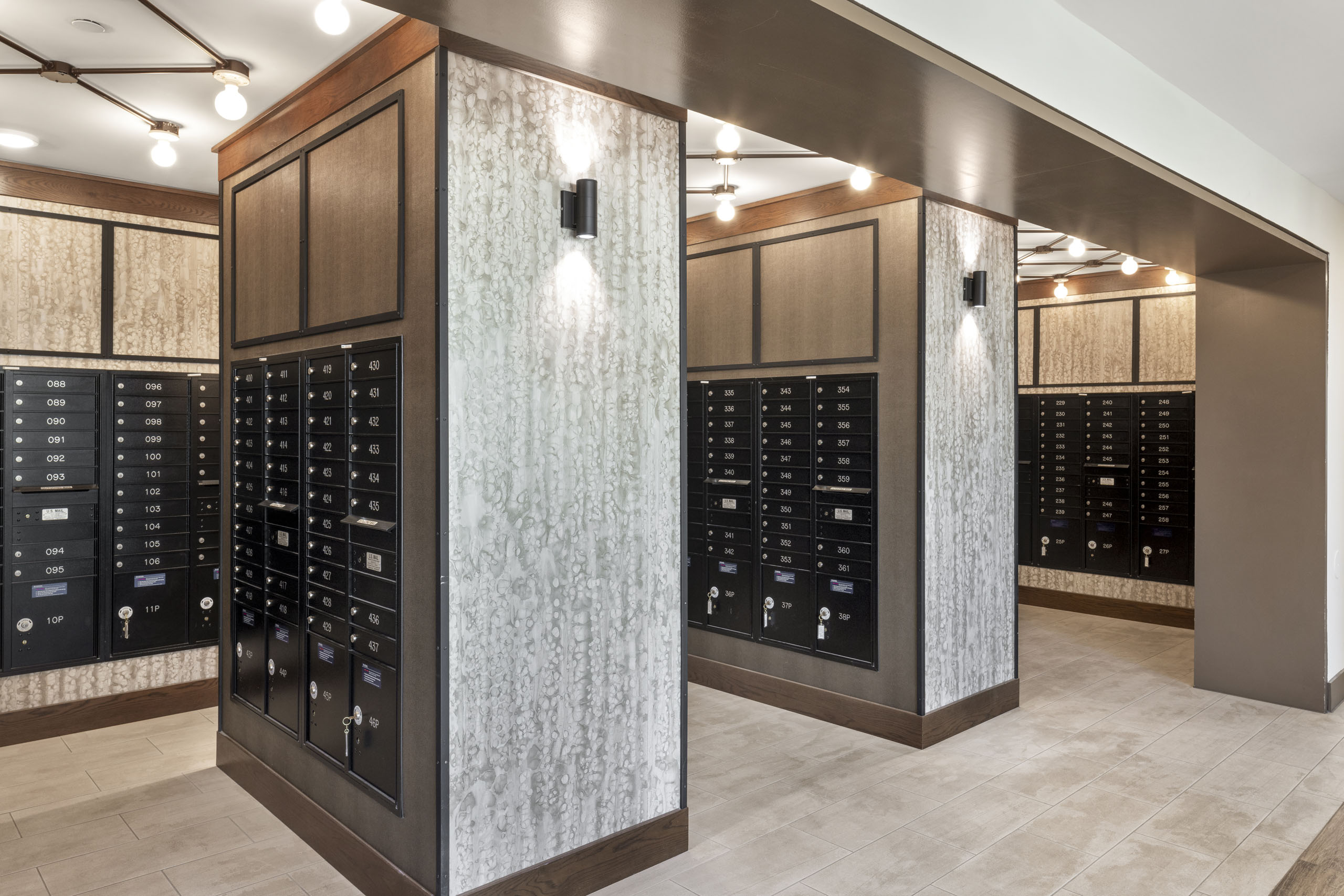View of AMLI Lakeline mailroom featuring black mail boxes with cream tile flooring and white and gray patterned walls