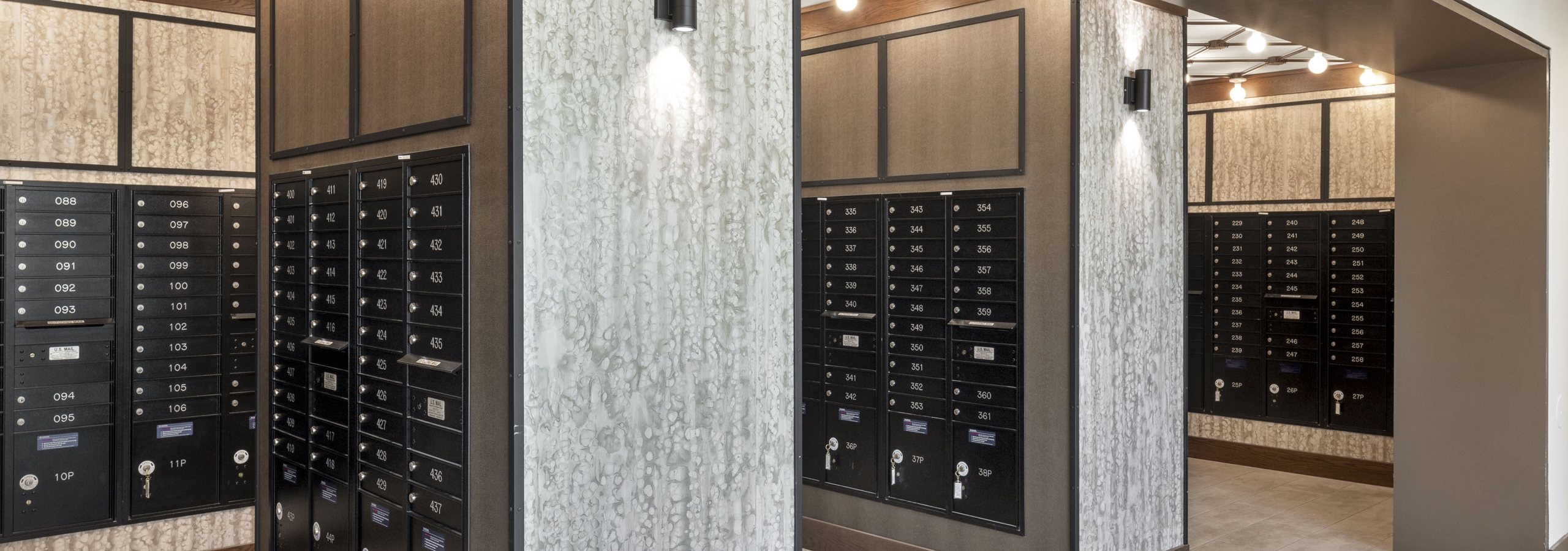 View of AMLI Lakeline mailroom featuring black mail boxes with cream tile flooring and white and gray patterned walls