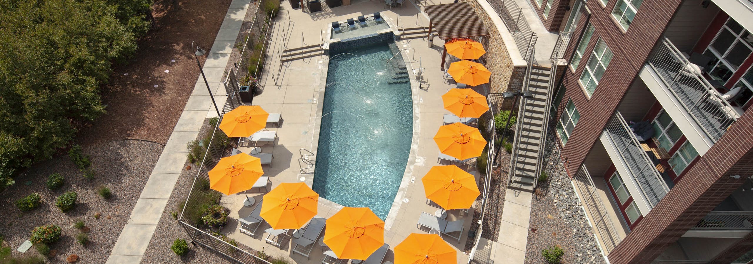 An aerial view of the pool at AMLI Dry Creek apartments with several orange umbrellas and landscaping with rocks and bushes