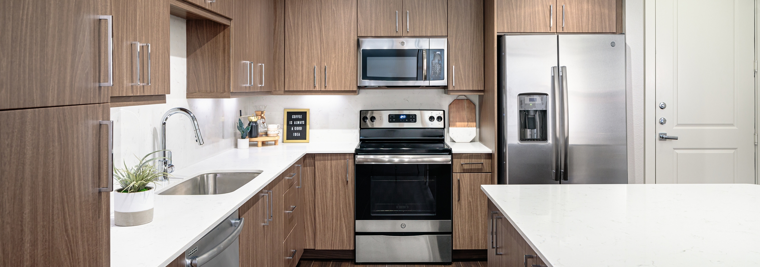 Interior close up of spacious AMLI Addison island kitchen with sleek quartz countertops and light wood cabinets