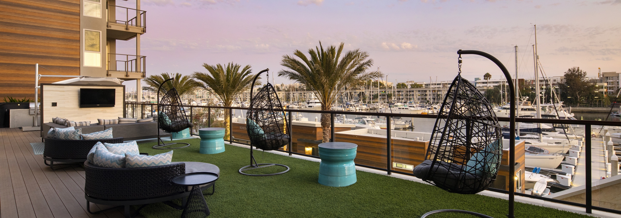 Daytime view of lounge with teardrop hanging chairs and big screen TV overlooking marina at AMLI Marina Del Rey apartments