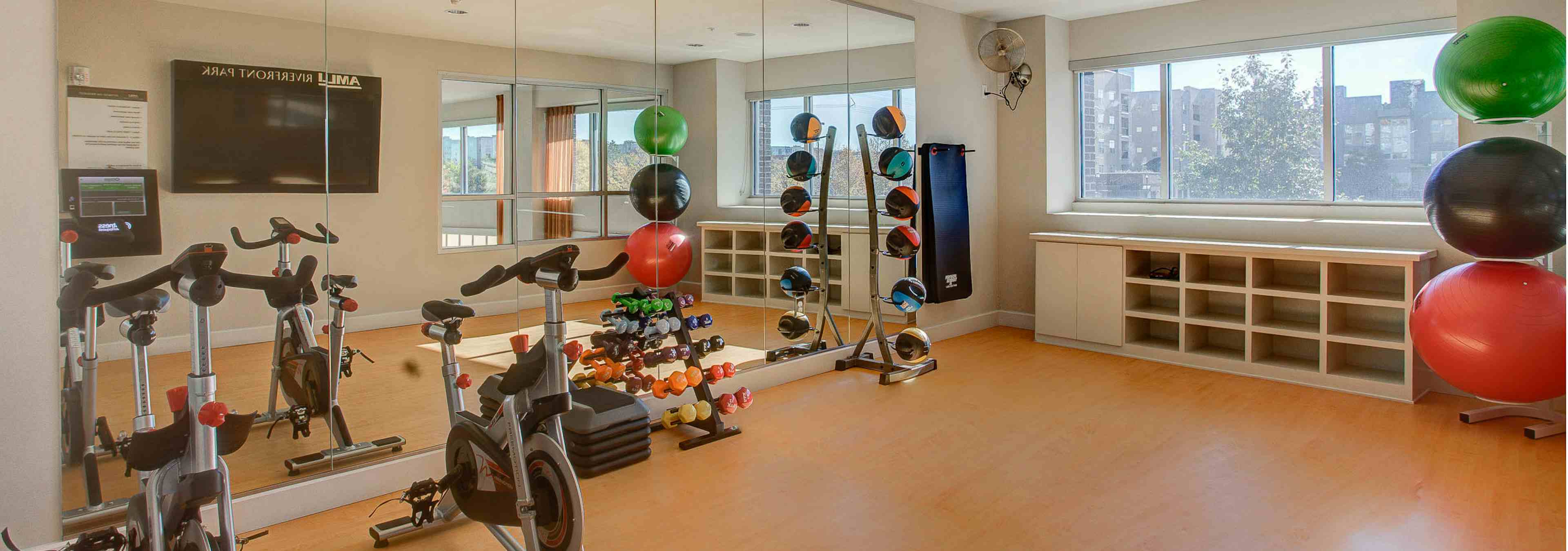 A yoga studio at AMLI Riverfront Park apartments with a floor to ceiling mirror and stationary bikes and weights and windows