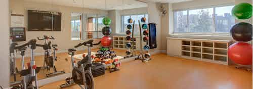 A yoga studio at AMLI Riverfront Park apartments with a floor to ceiling mirror and stationary bikes and weights and windows