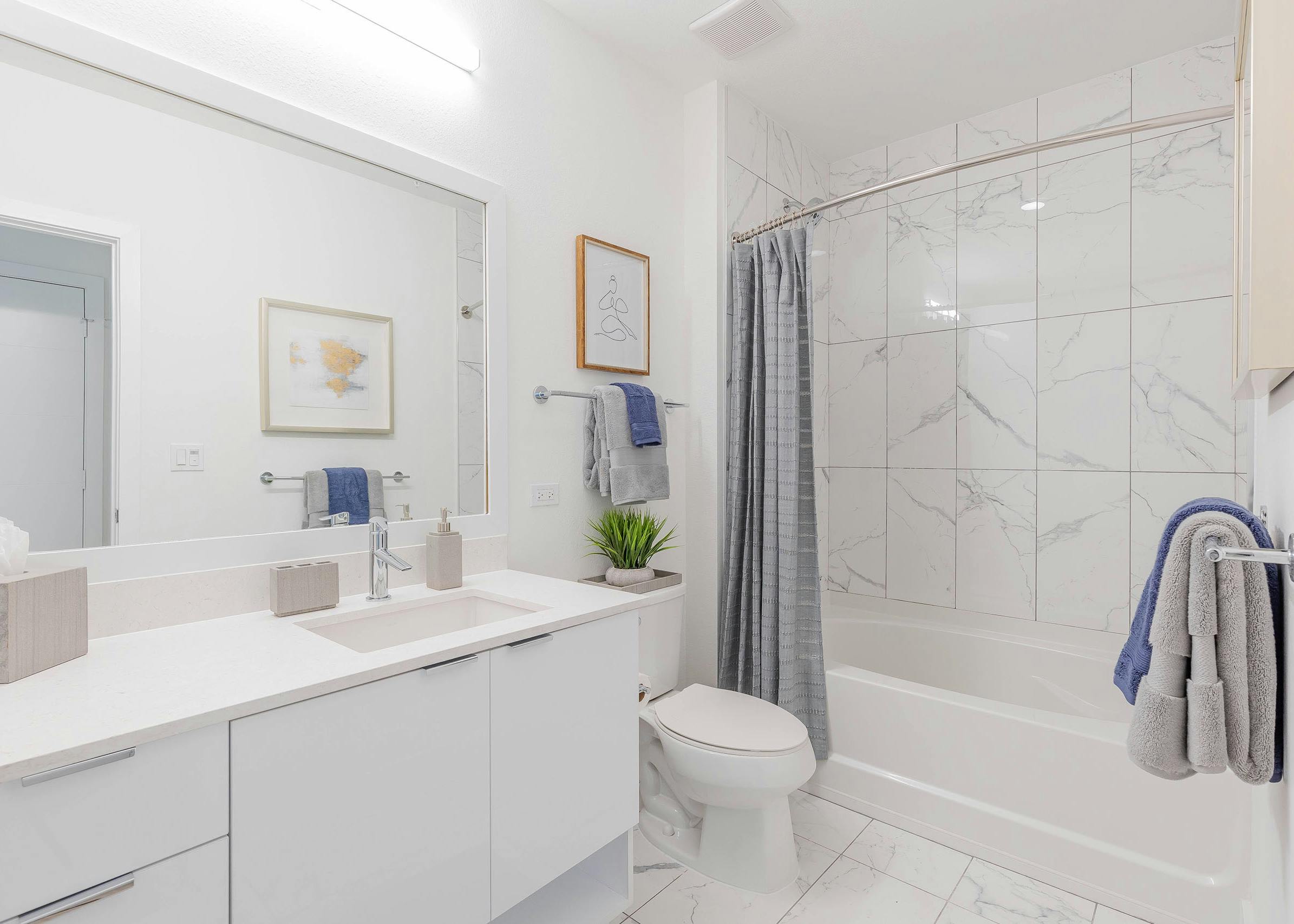 AMLI Park West apartment bedroom with gray bedding on low profile bed with two brown wood nightstands and view of bathroom