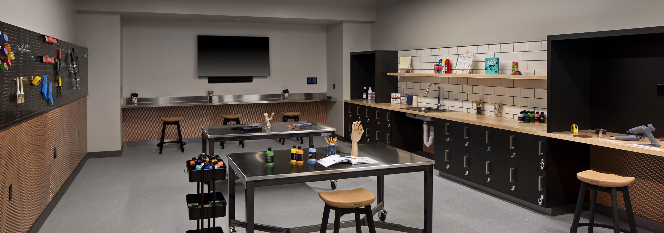 Interior view of makers lab displaying an array of tools for crafts and a big screen TV at AMLI Old Pasadena apartments