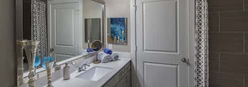 AMLI Eastside apartment bathroom with quartz countertops and large mirror and lights above and closed door and garden tub