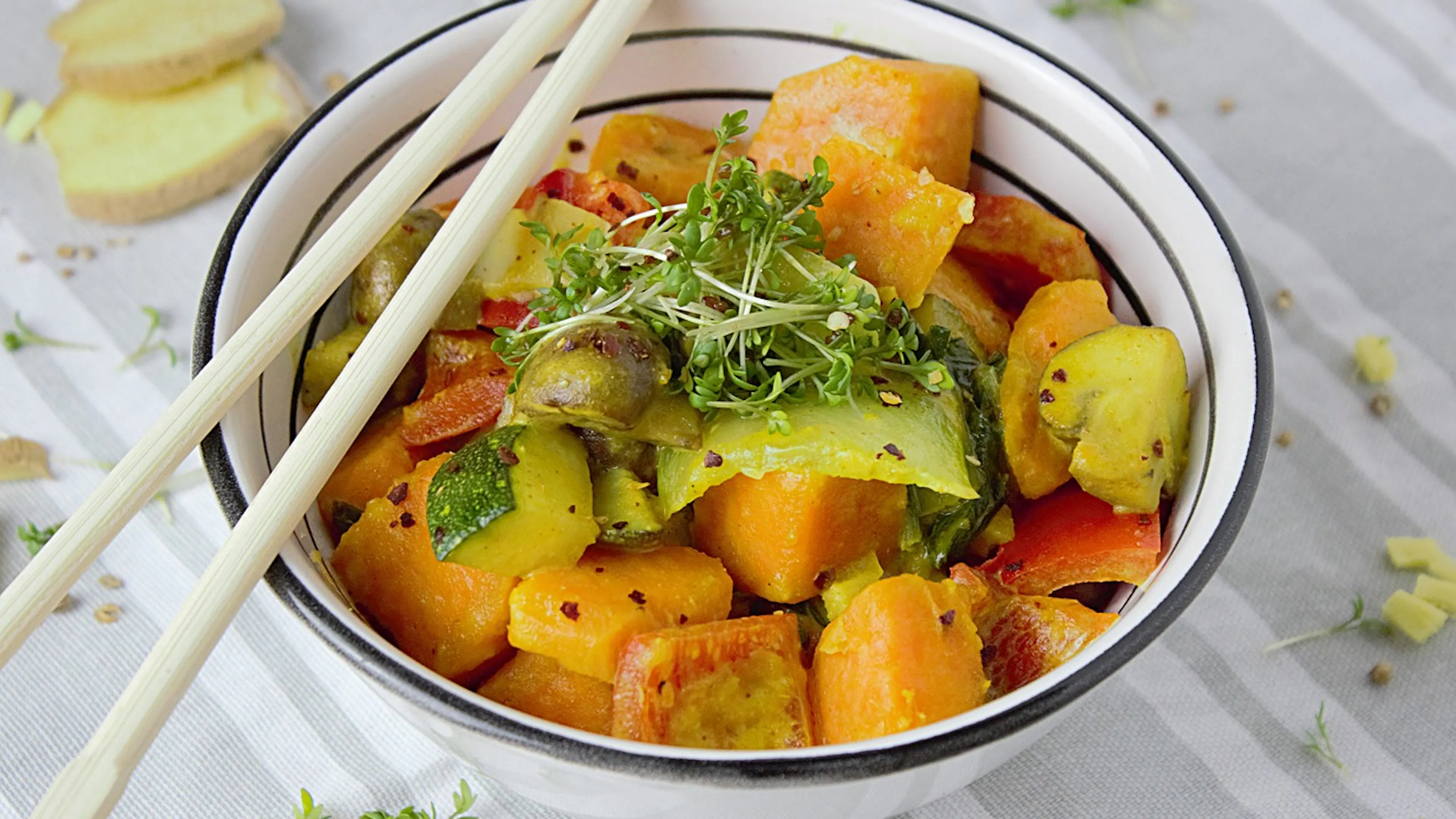 White and black ceramic bowl filled with curried vegetables and garnished with bean sprouts and two chopsticks