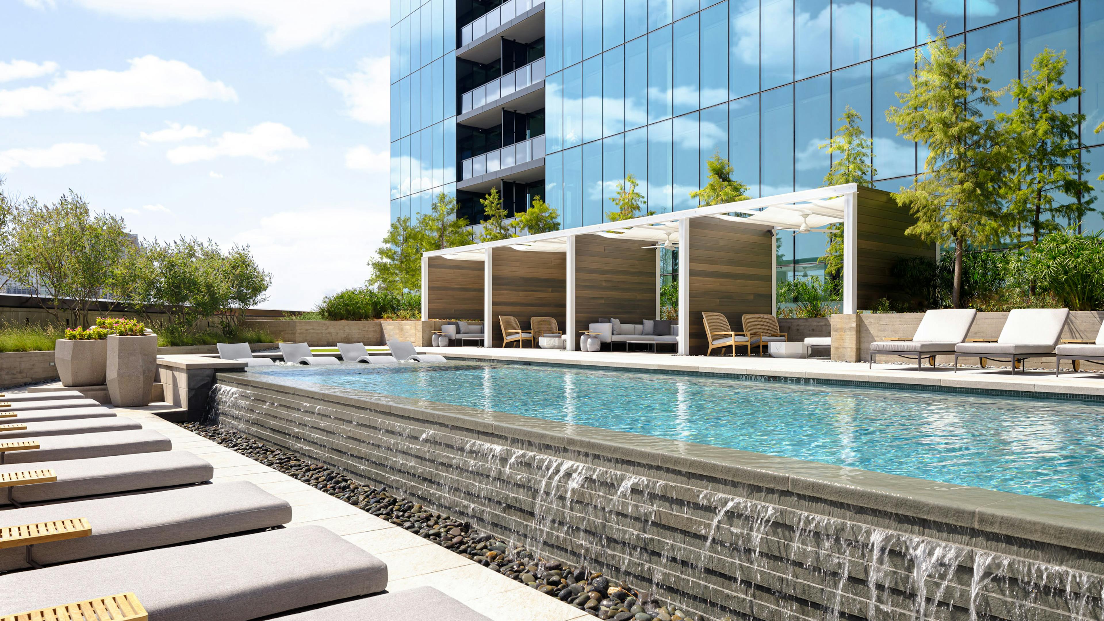AMLI Fountain Place pool with infinity edge waterfall cascading on grey stones with grey lounge chairs and private cabanas