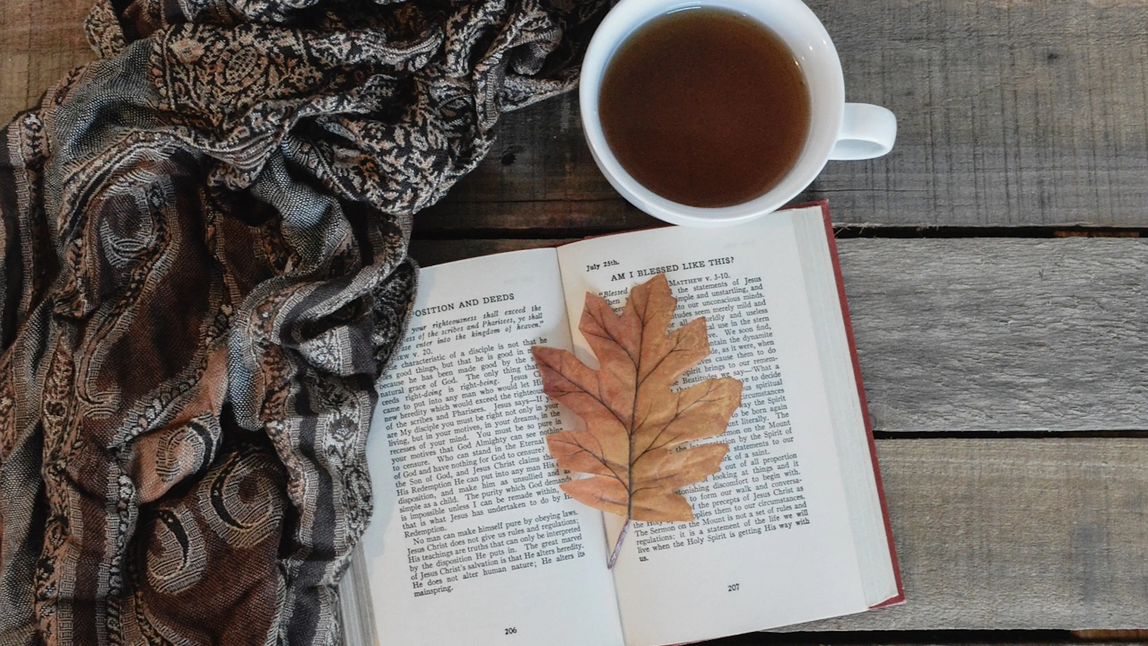 multicolored scarf with open book and autumn leaf and cup of tea on wood slats