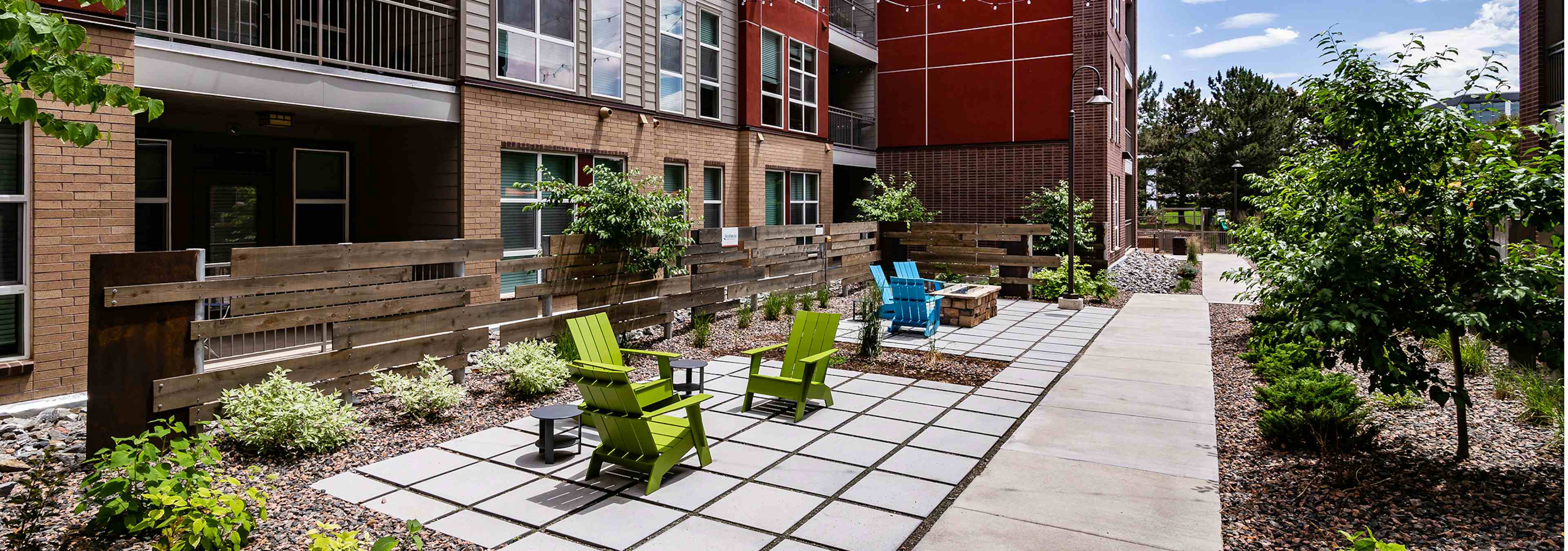 Exterior view of a courtyard area at AMLI Dry Creek apartments with lounge chairs with wood chip landscaping and many trees 