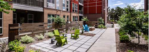Exterior view of a courtyard area at AMLI Dry Creek apartments with lounge chairs with wood chip landscaping and many trees