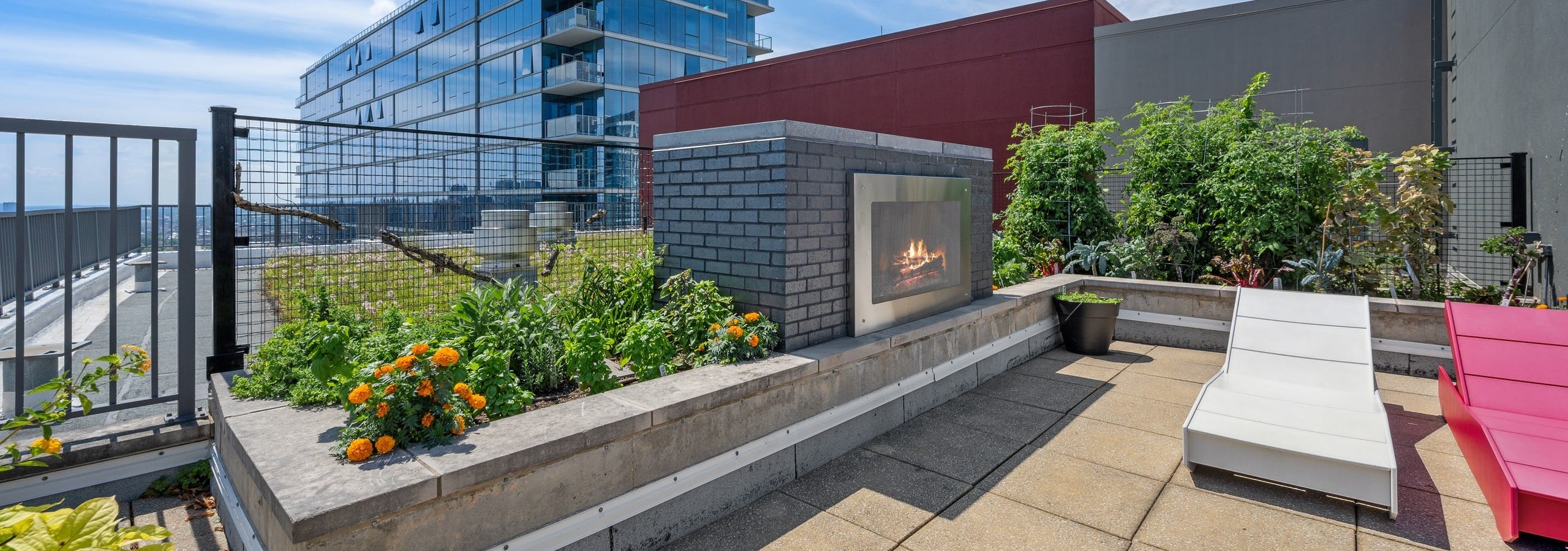 Large outdoor fireplace at AMLI 900 apartment building with rooftop vegetable garden and red and white lounge chairs