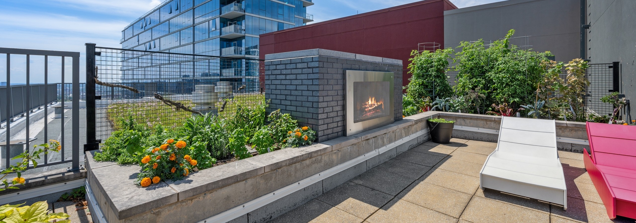 Large outdoor fireplace at AMLI 900 apartment building with rooftop vegetable garden and red and white lounge chairs