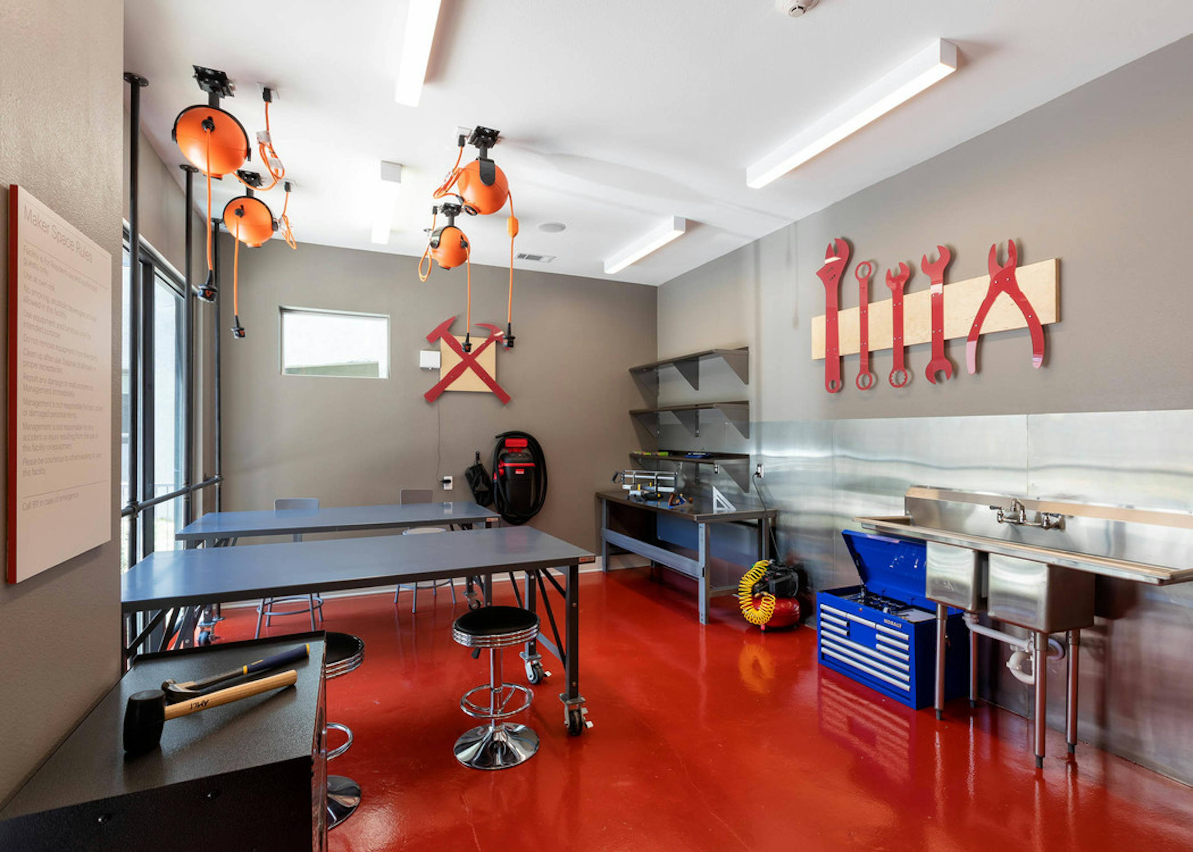 Makers space at AMLI on Aldrich with grey table and chairs and different stations with red tools on walls for creating
