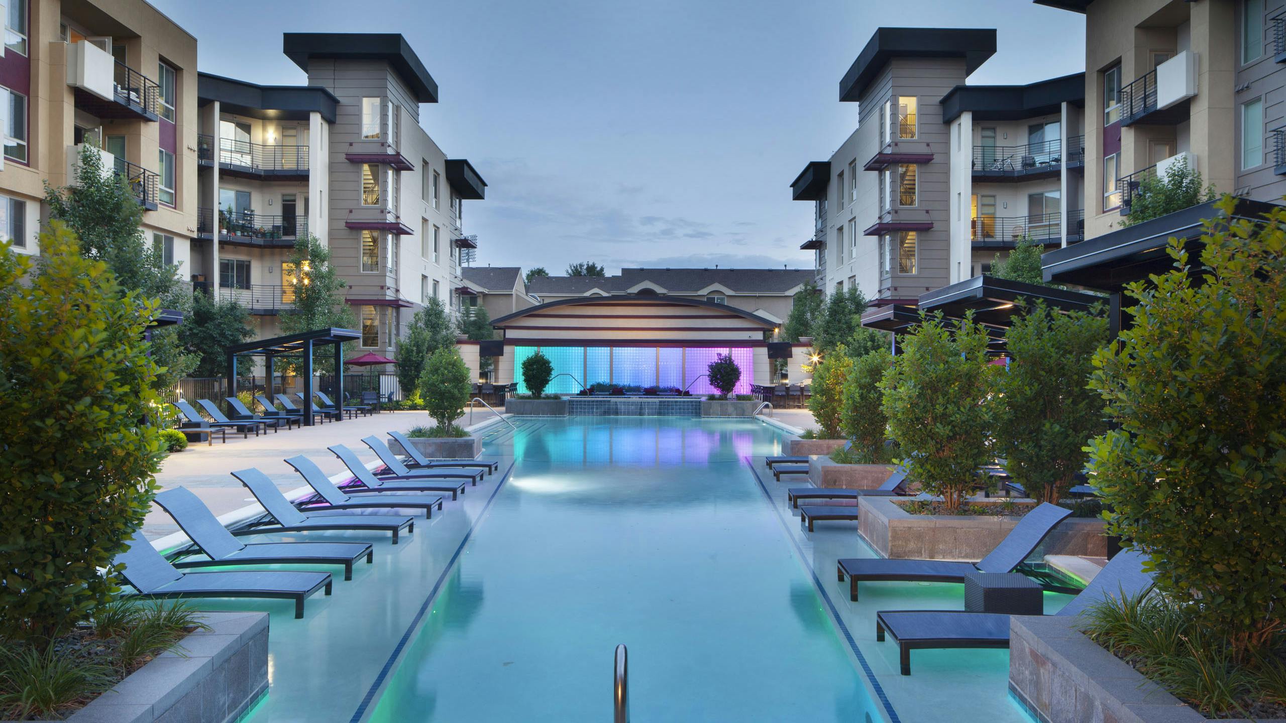 Evening view at AMLI Cherry Creek pool with lounge seating and cabanas and lush plants as well as a hot tub and waterfall