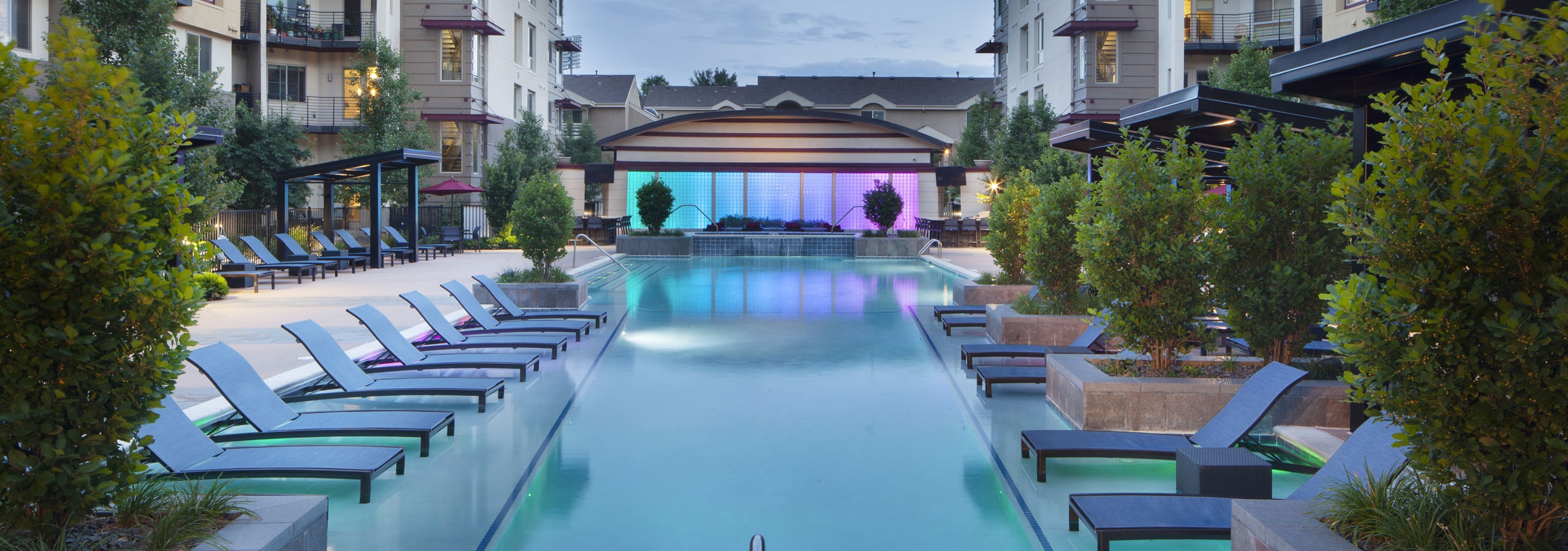 Evening view at AMLI Cherry Creek pool with lounge seating and cabanas and lush plants as well as a hot tub and waterfall