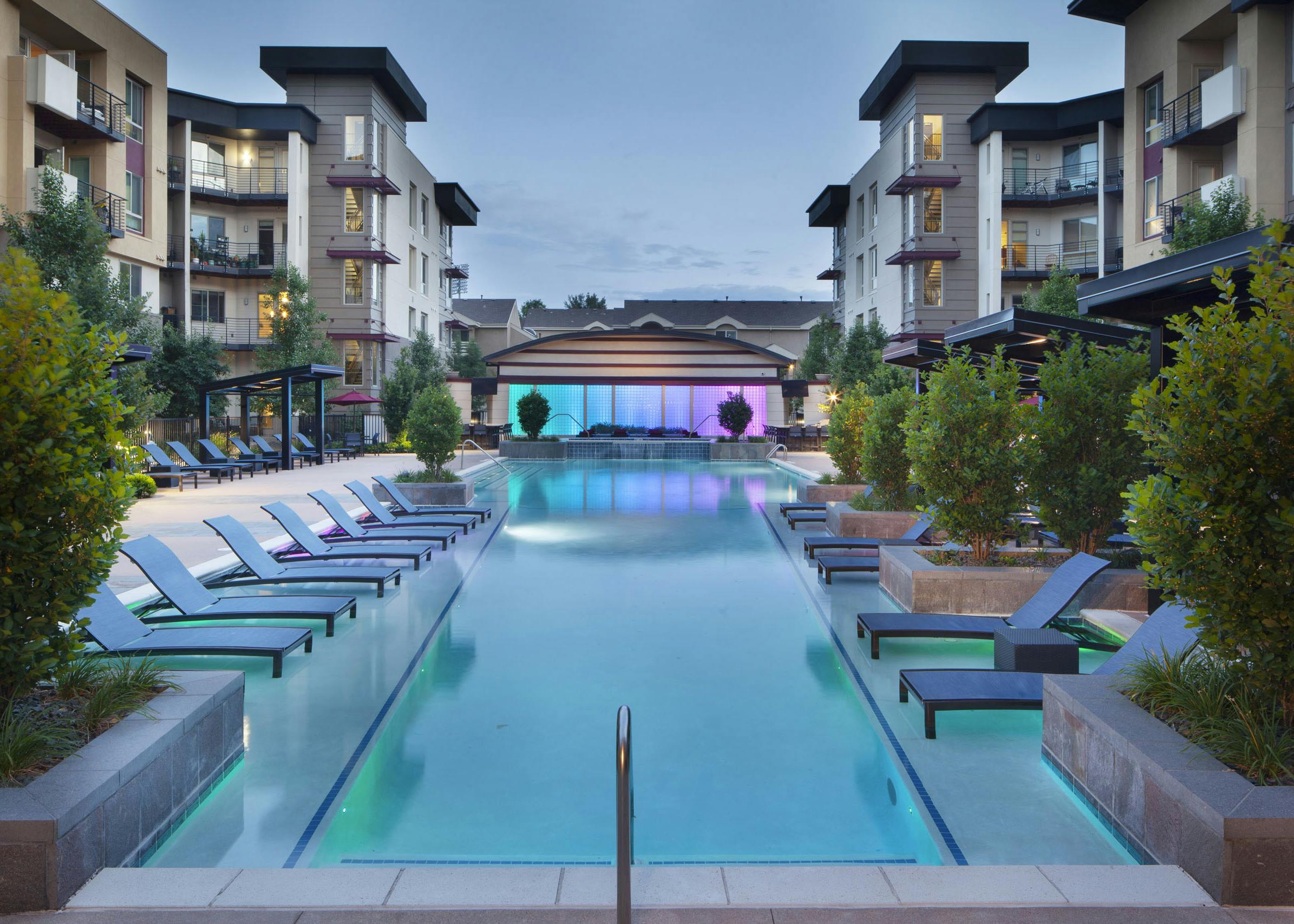 Evening view at AMLI Cherry Creek pool with lounge seating and cabanas and lush plants as well as a hot tub and waterfall