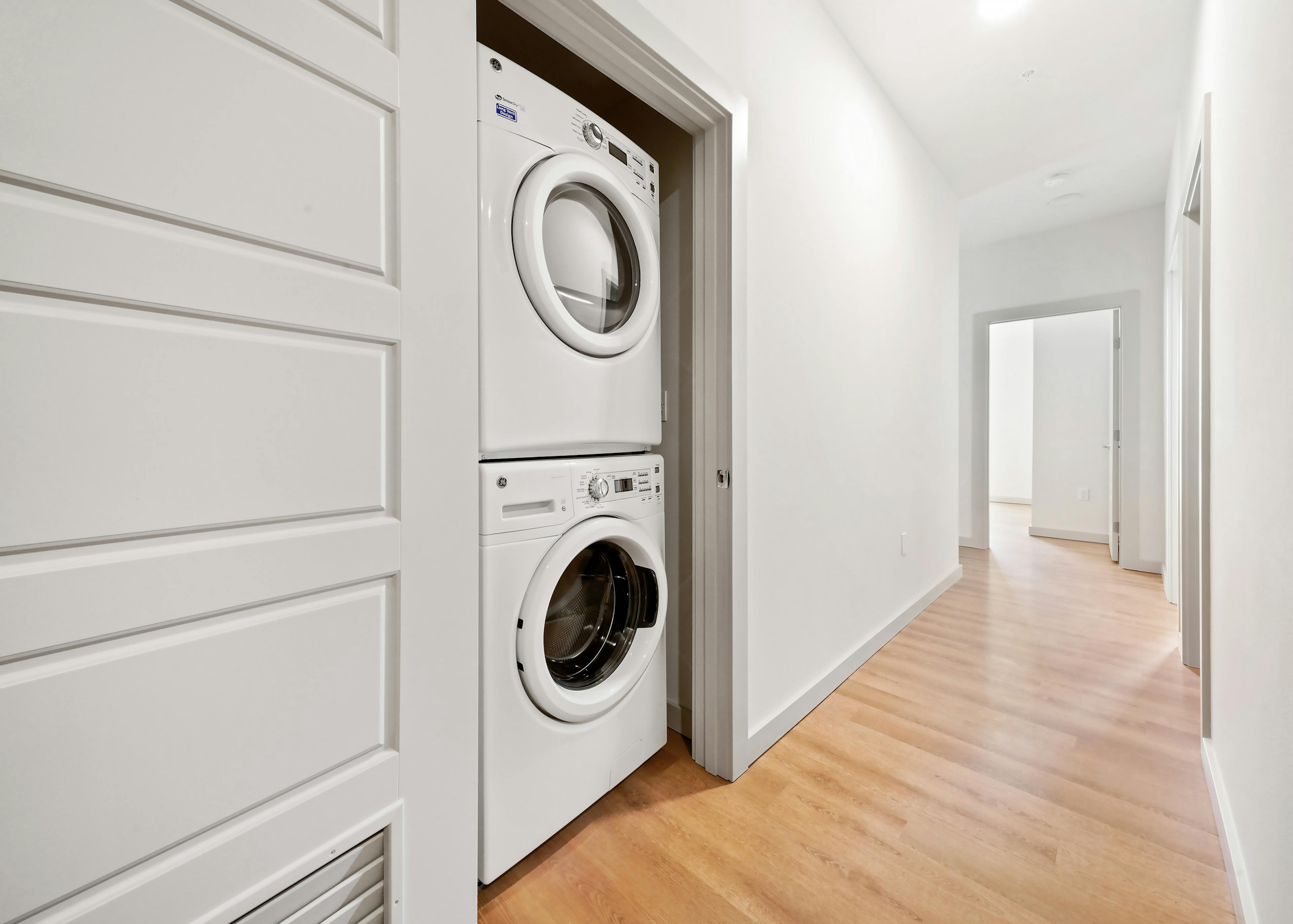 Interior view of stackable washer and dryer in an AMLI Spring District apartment with long hallway leading to bedrooms