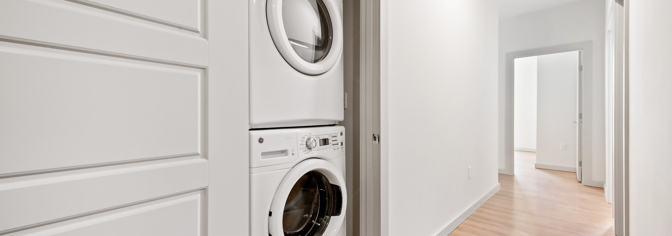 Interior view of stackable washer and dryer in an AMLI Spring District apartment with long hallway leading to bedrooms