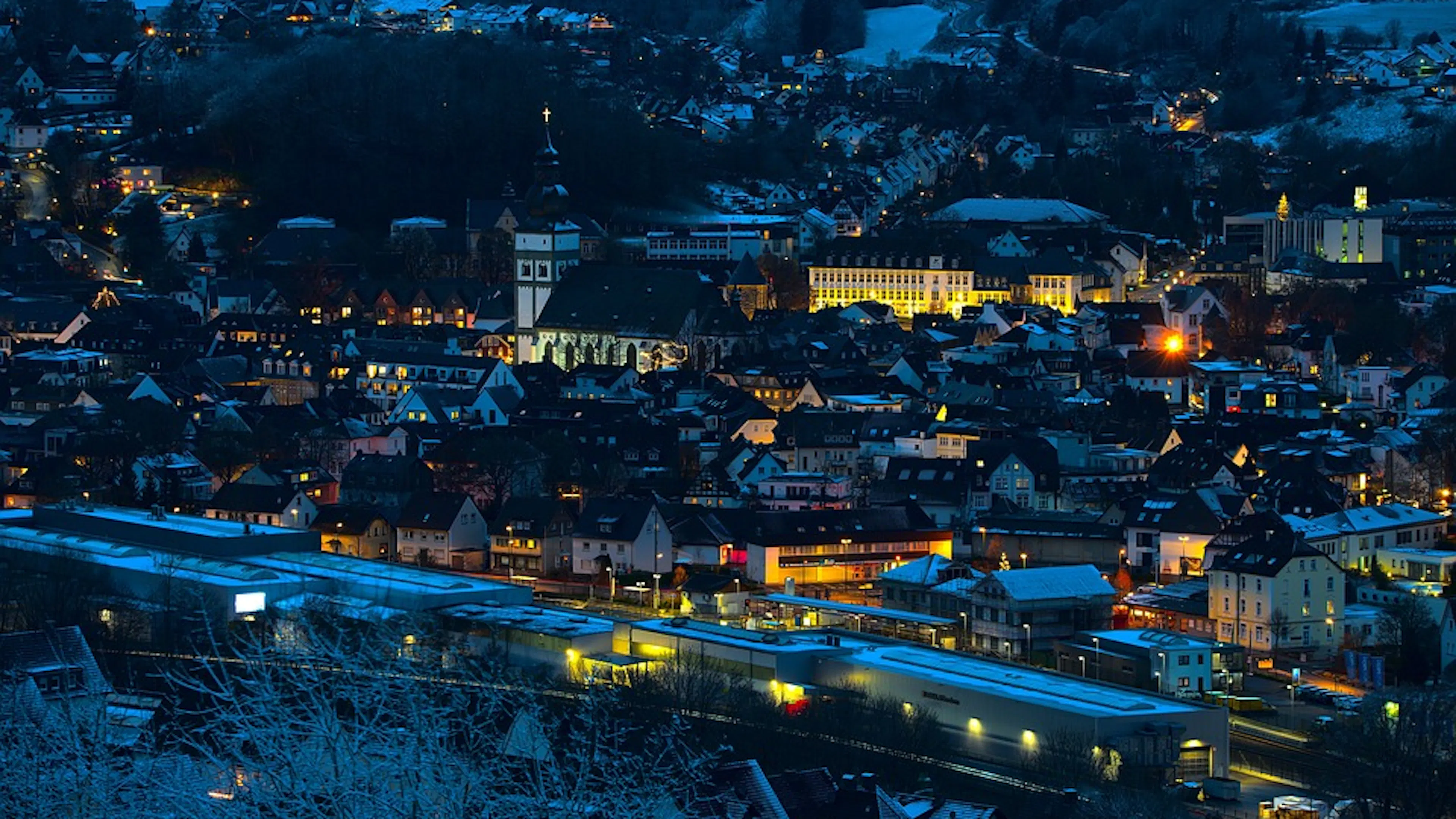 A town at night lit up by soft lights and snow covering the roofs and meadows around it