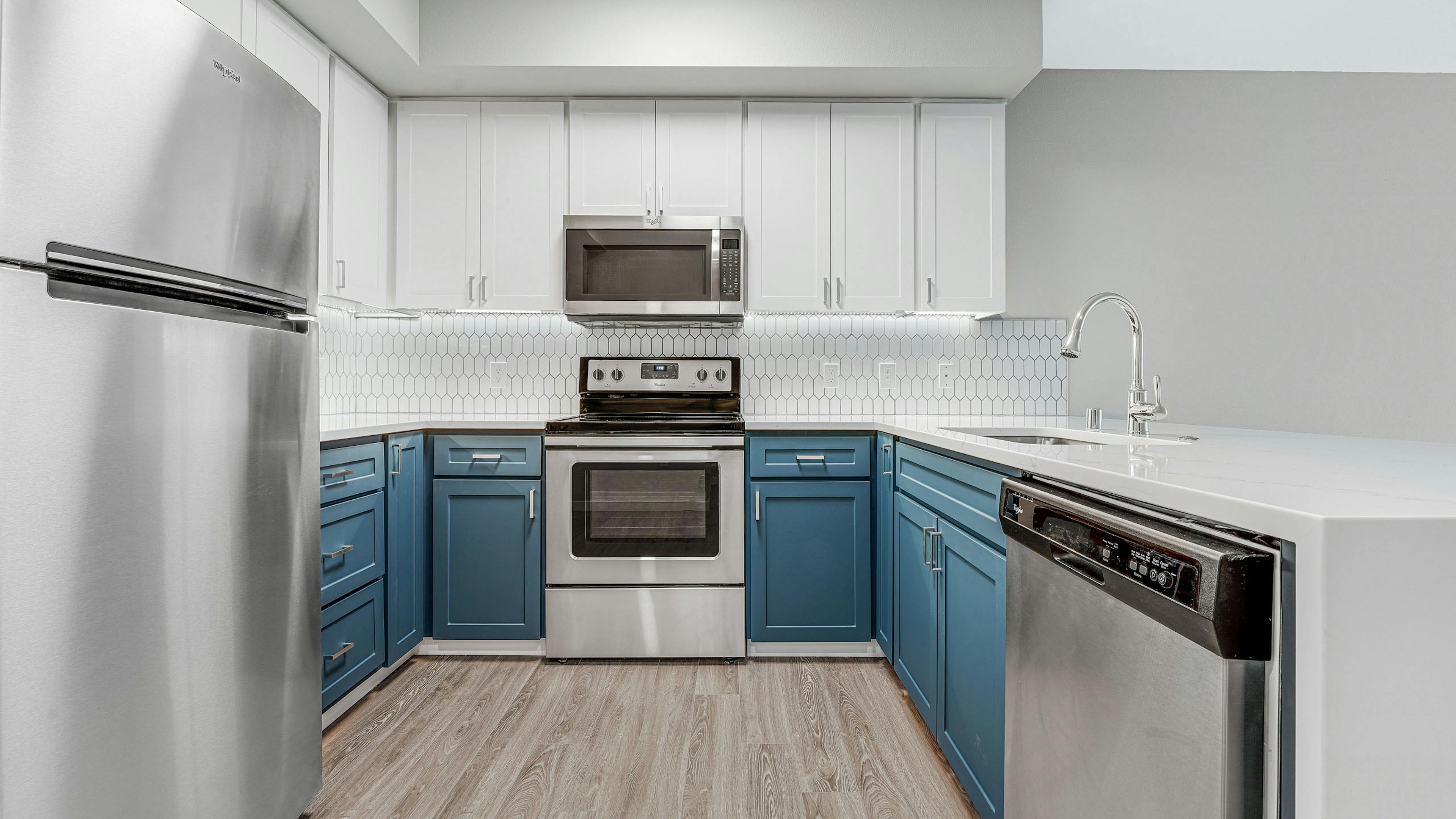 Kitchen at AMLI 535 apartment building with white and blue cabinets and stainless steel appliances with light gray floors