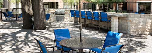 Outdoor barbecue area at AMLI Eastside with round tables and blue chairs with blue barstools at a brick counter in background