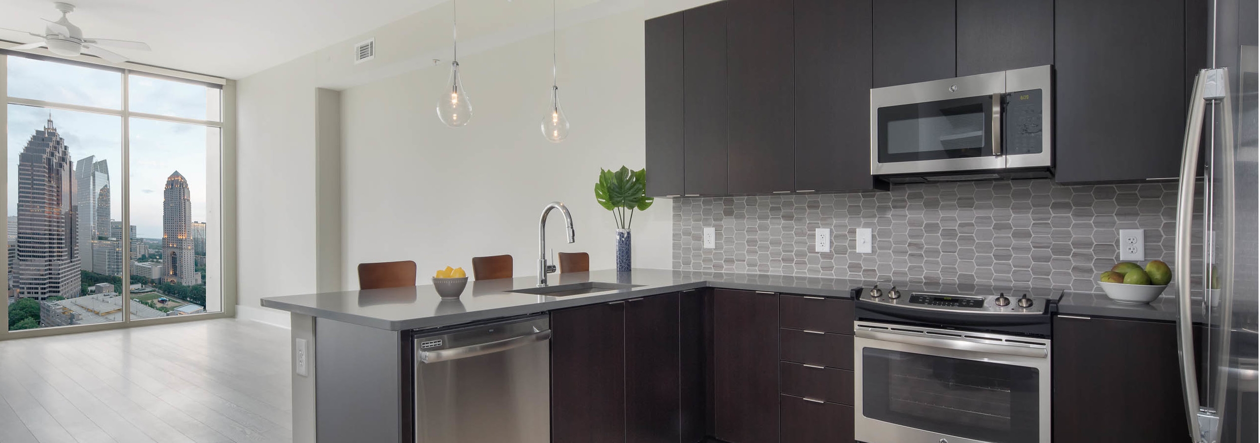 Kitchen at AMLI Arts Center with light wood floor leading to living area with floor to ceiling windows with bright city view