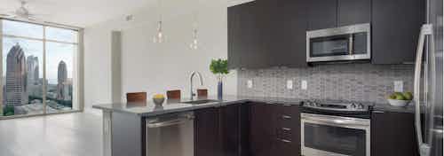 Kitchen at AMLI Arts Center with light wood floor leading to living area with floor to ceiling windows with bright city view