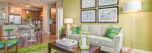 A living room at AMLI Riverfront Park apartments with couches and lamps and a green color scheme with a view into the kitchen