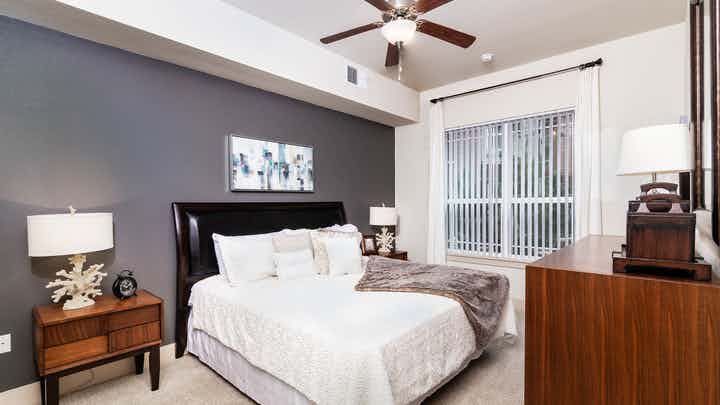 Interior view of a bedroom at AMLI Park Avenue apartments with a bed with black head board and lamps with glass balcony door