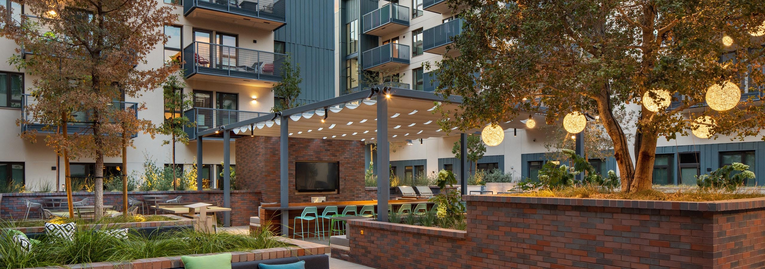 Landscaped courtyard at dusk with fire pit and various lounge seating and big screen TV at AMLI Old Pasadena apartments