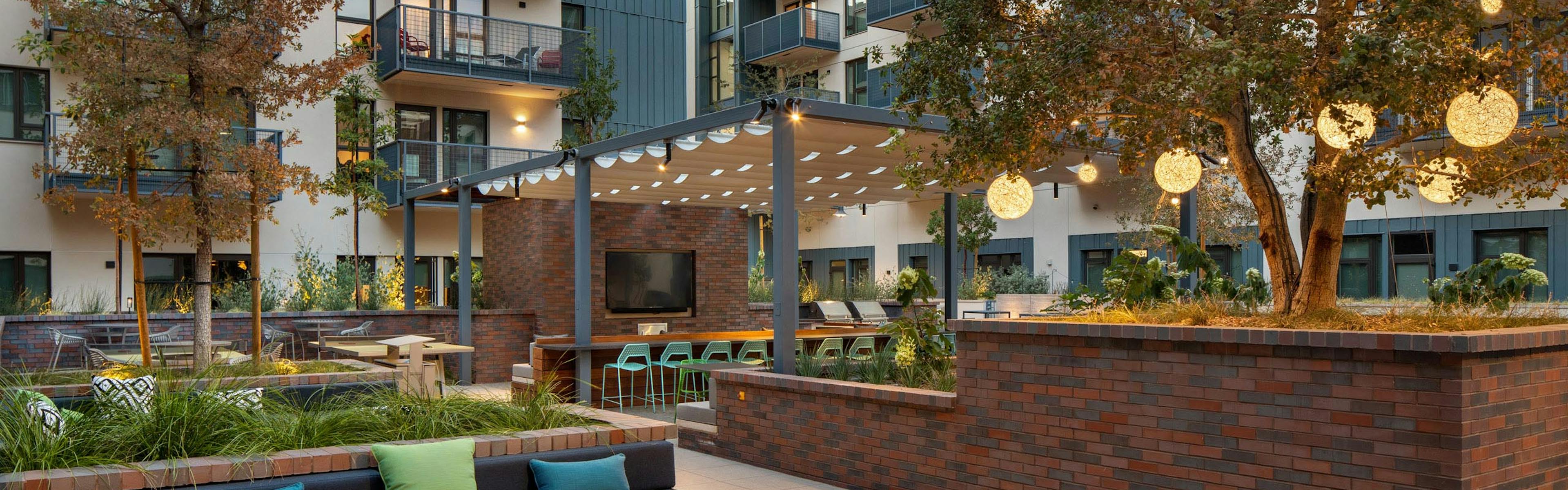 Landscaped courtyard at dusk with fire pit and various lounge seating and big screen TV at AMLI Old Pasadena apartments
