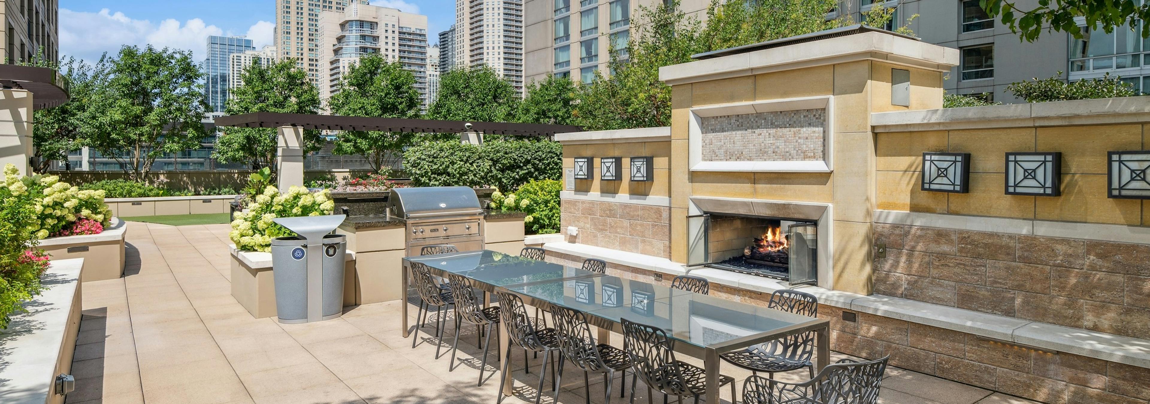 View of large outdoor fireplace with long dining table and grilling station with view of city skyline at AMLI River North