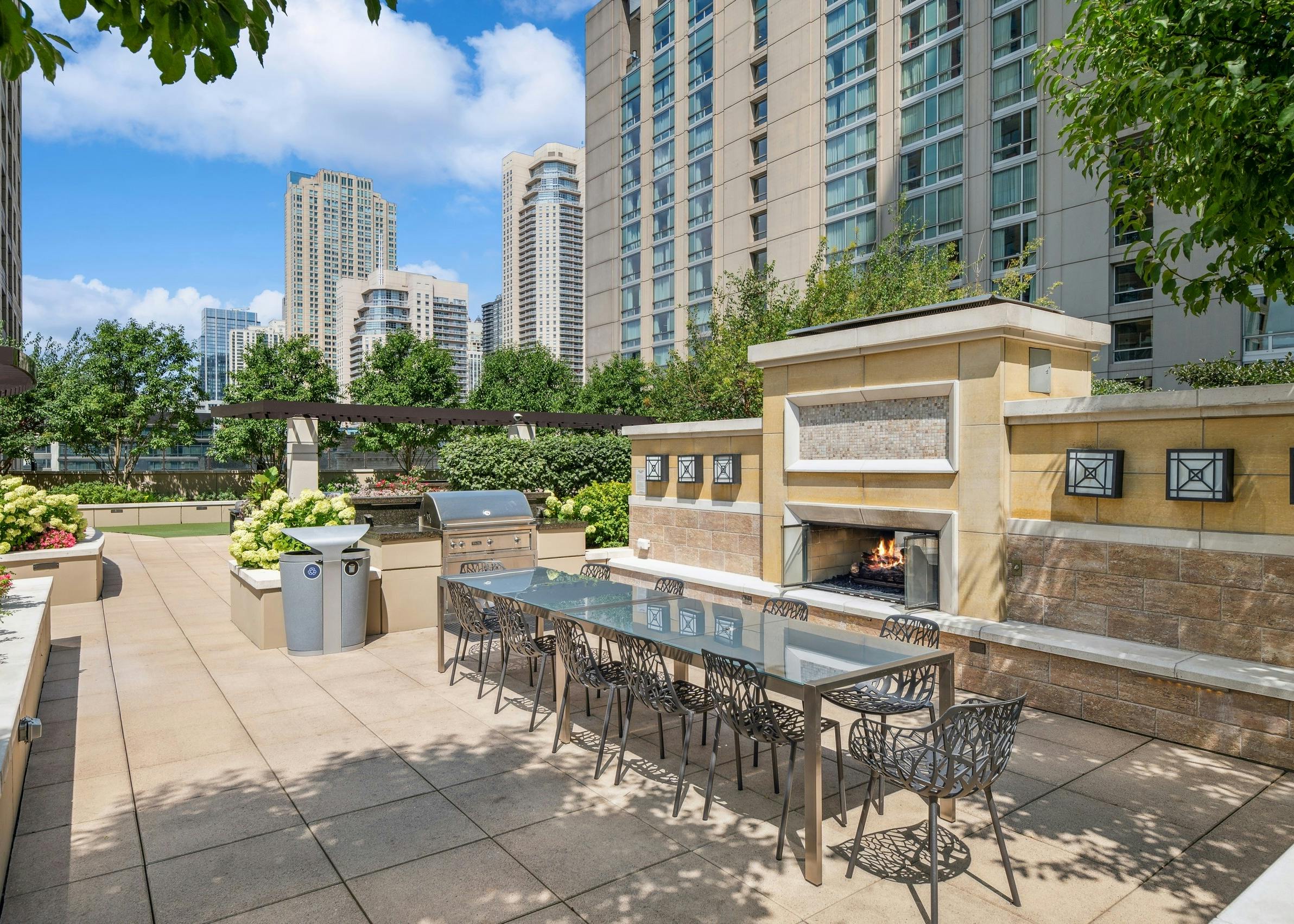 View of large outdoor fireplace with long dining table and grilling station with view of city skyline at AMLI River North